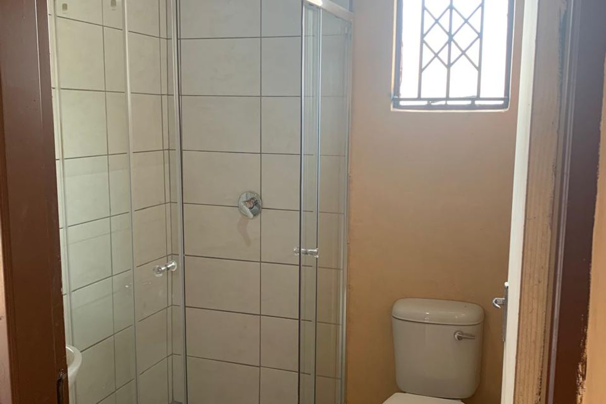 A compact bathroom featuring a glass shower enclosure, a standard toilet, and tiled finishes, requiring minor cosmetic updates to the door frame and walls.