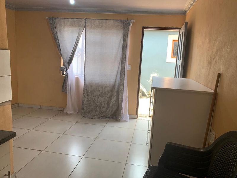 A living area featuring tiled flooring and direct access to an outdoor space, requiring cosmetic updates to the wall finishes.