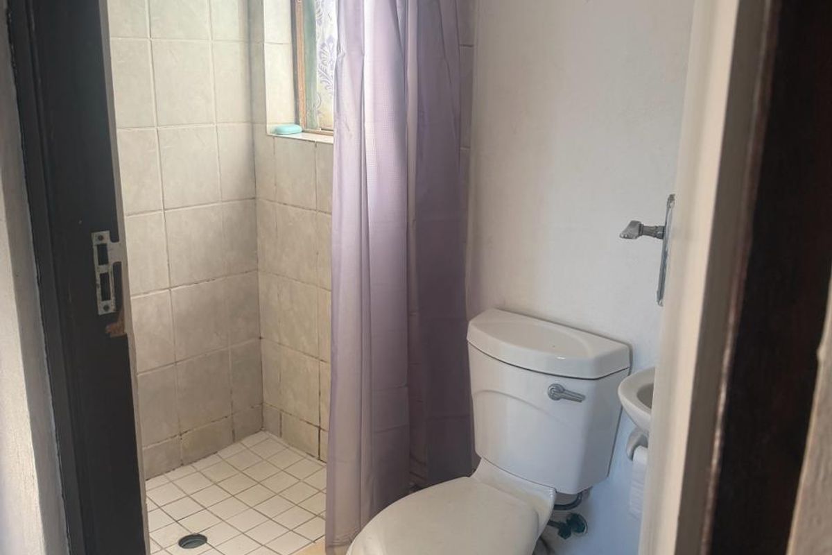 A compact bathroom featuring a shower cubicle, toilet, and wall-mounted basin with neutral tiled finishes.