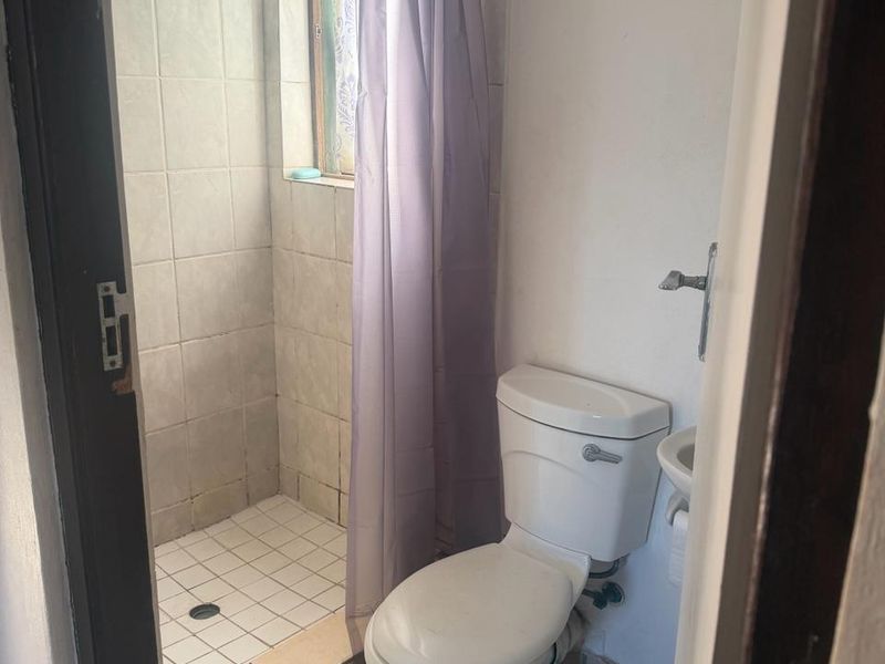 A compact bathroom featuring a shower cubicle, toilet, and wall-mounted basin with neutral tiled finishes.