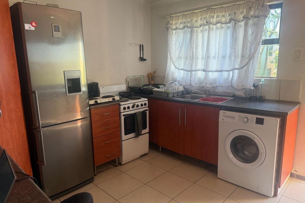 A functional kitchen featuring wood-tone cabinetry, laminate countertops, a stainless steel sink, and tiled flooring, offering a practical layout for daily use.