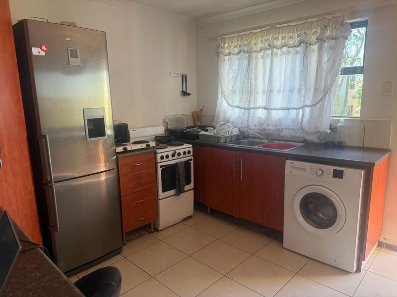 A functional kitchen featuring wood-tone cabinetry, laminate countertops, a stainless steel sink, and tiled flooring, offering a practical layout for daily use.