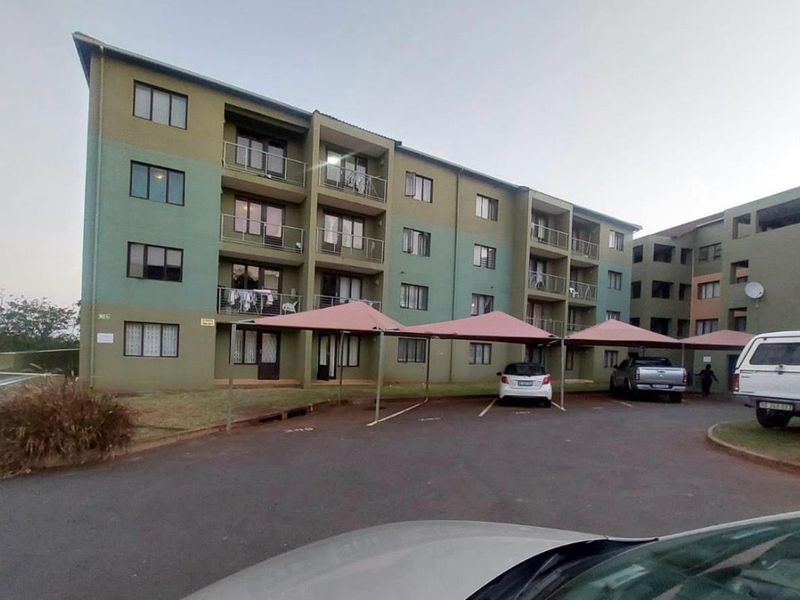 Exterior view of a multi-story apartment complex featuring private balconies and covered parking bays for residents.