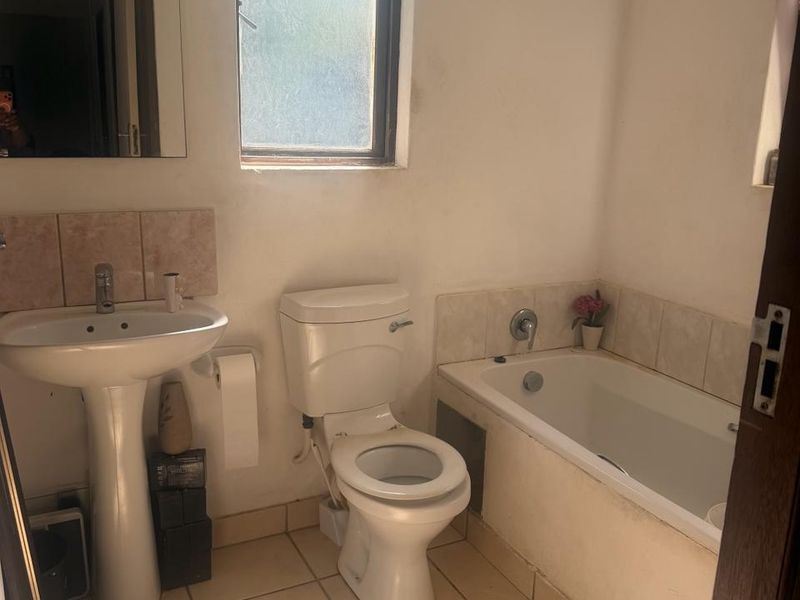 A functional bathroom featuring a pedestal basin, standard toilet, and a bathtub with tiled splashbacks and flooring.