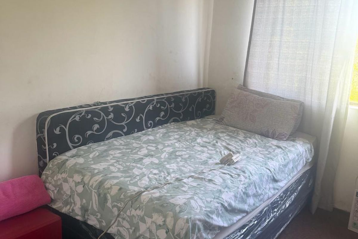A bedroom featuring a window with a curtain rail, showing signs of wear on the walls and carpet.