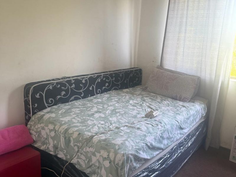 A bedroom featuring a window with a curtain rail, showing signs of wear on the walls and carpet.