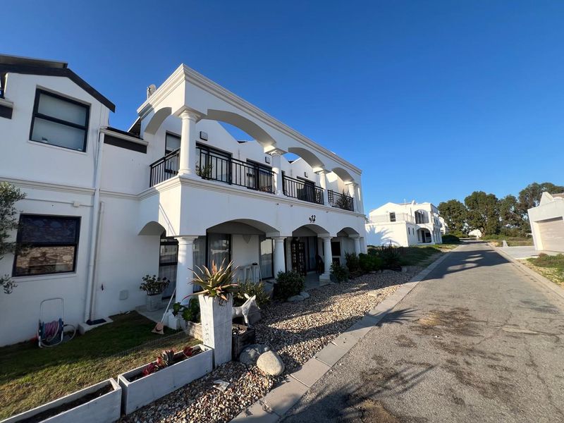 Front elevation of a multi-story residential property featuring a distinctive arched colonnade, upper-level balcony with metal railings, and a paved driveway.