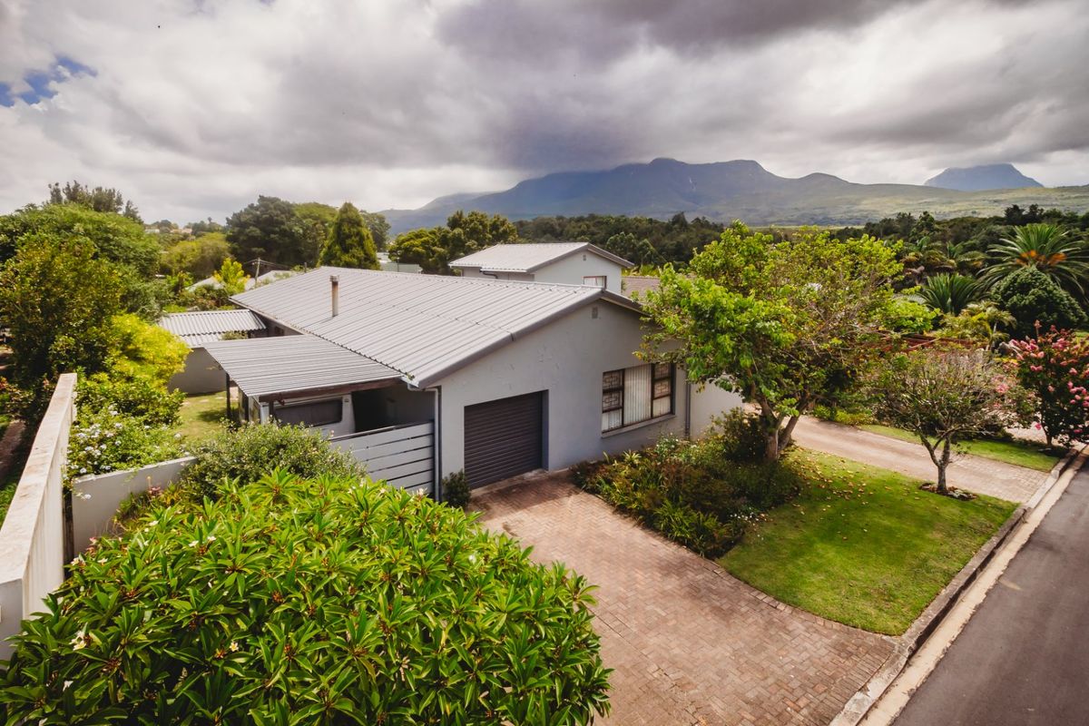 Aerial view of a residential property featuring a metal roof, brick paved driveway, and garage, set against a scenic mountain backdrop.