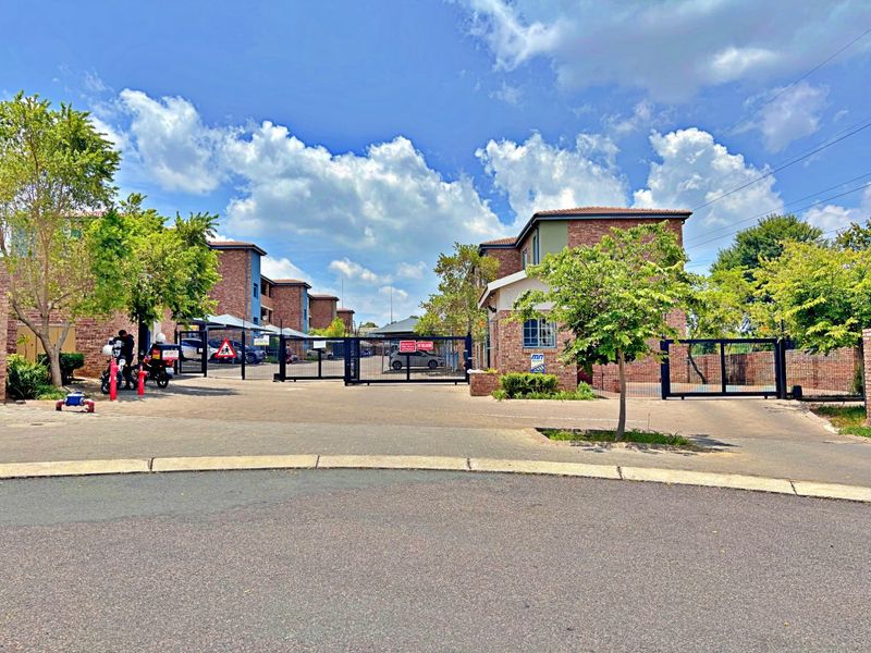 Front view of the apartment complex entrance featuring a secure gated access point, brick building facades, and paved driveway.