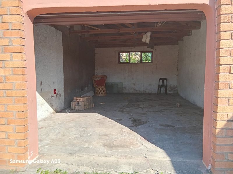 A spacious, unfinished garage featuring exposed timber roof trusses, concrete flooring, and brick masonry walls, offering potential for storage or workshop conversion.