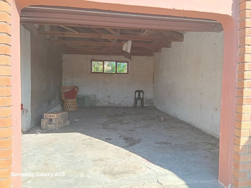 A spacious, unfinished garage featuring exposed timber roof trusses, concrete flooring, and brick masonry walls, offering potential for storage or workshop conversion.