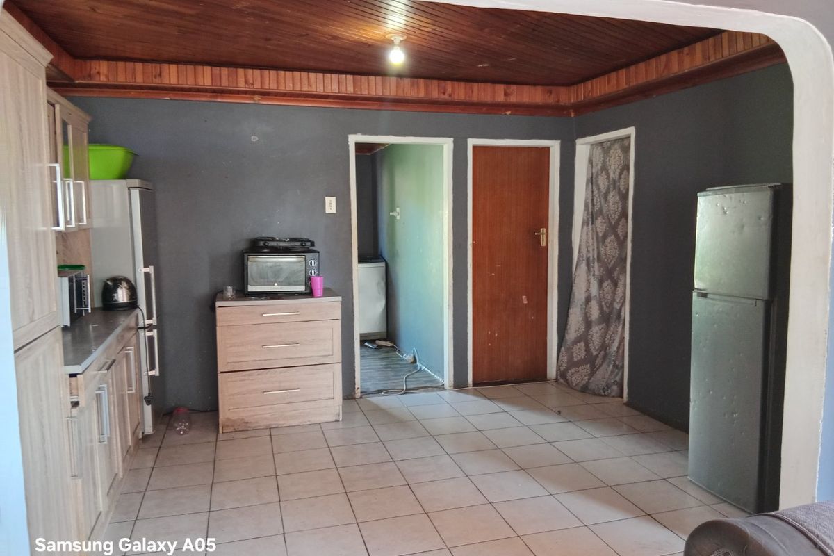 A functional kitchen area featuring tiled flooring, timber ceiling paneling, and built-in cabinetry with laminate countertops, offering potential for modernization.