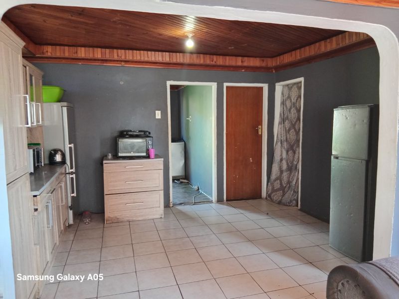A functional kitchen area featuring tiled flooring, timber ceiling paneling, and built-in cabinetry with laminate countertops, offering potential for modernization.