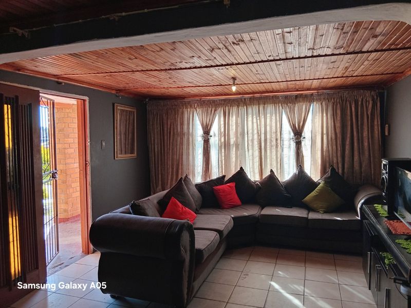 A living room featuring a timber-clad ceiling, ceramic tiled flooring, and direct access to an exterior area through a security gate.