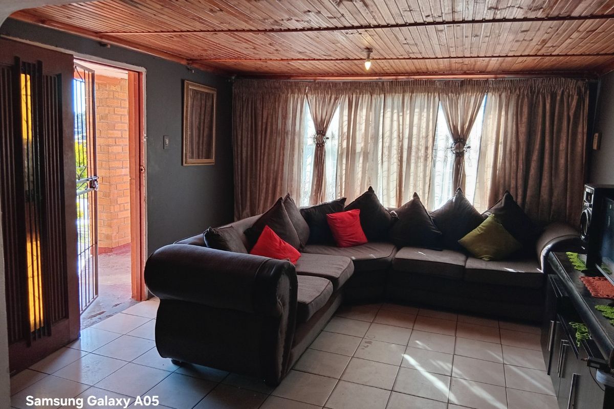 A living room featuring tiled flooring and a timber tongue and groove ceiling, with direct access to an outdoor area via a security gate.
