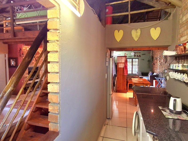 Open plan living area featuring exposed brick walls, timber roof trusses, a mezzanine level with a wooden staircase, and a kitchen with granite countertops.