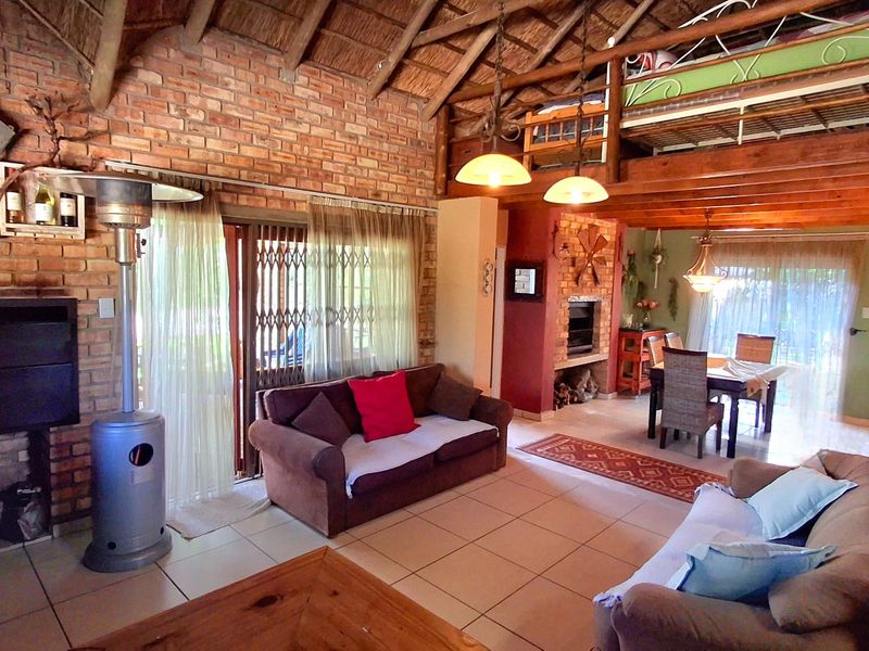 Spacious open-plan living and dining area featuring exposed brick walls, a high thatched ceiling, a mezzanine level, and a built-in fireplace.