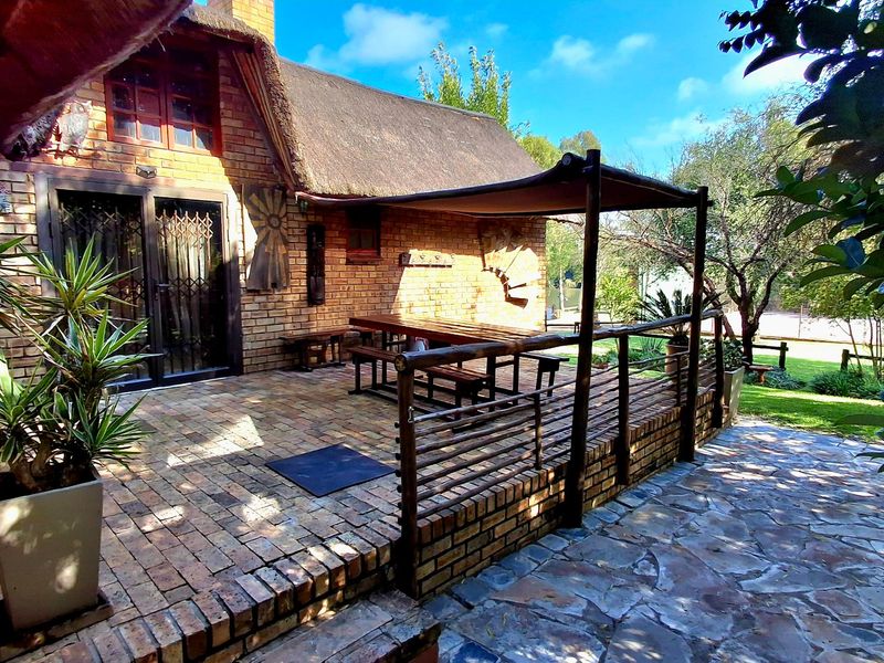 A charming outdoor patio area featuring brick paving, a thatched roof overhang, and a shade sail, providing a comfortable space for outdoor relaxation.