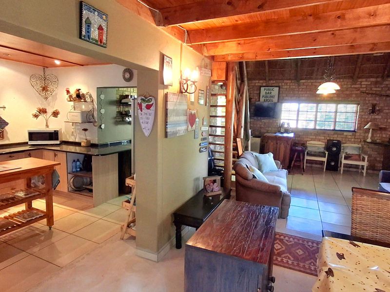 Open-plan living area featuring exposed timber beams, brick feature wall, and a functional kitchen with granite countertops and tiled flooring throughout.