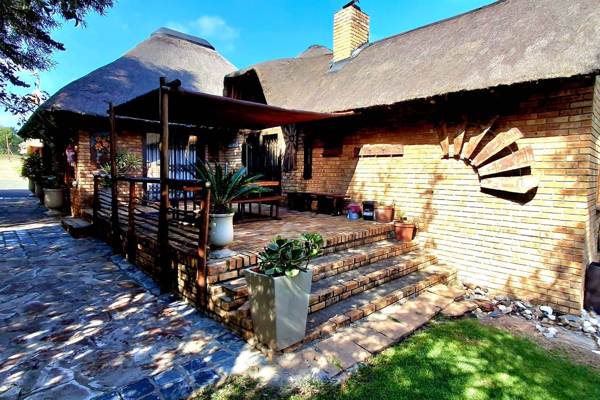 A charming rear exterior view featuring a traditional thatched roof, exposed brick walls, and a spacious brick-paved patio area with a timber pergola.