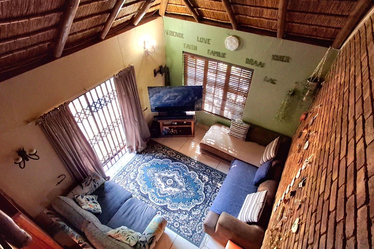 A cozy living room featuring an exposed thatch ceiling, a rustic brick feature wall, and tiled flooring with access to the exterior.