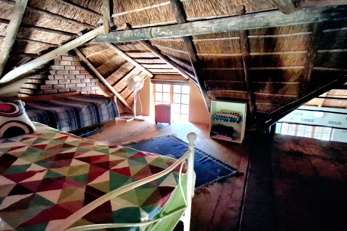 Loft-style bedroom featuring exposed timber rafters, a traditional thatched roof, and rustic brickwork, providing a unique architectural character.