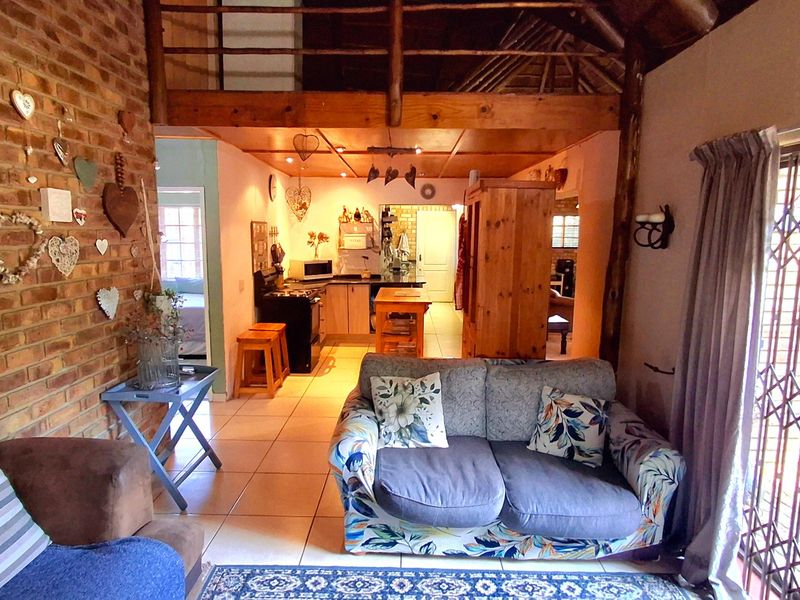 Open-plan living area featuring exposed brick walls, timber ceiling beams, a mezzanine level, and an integrated kitchen space with tiled flooring.