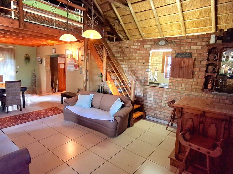 Spacious open-plan living area featuring a rustic brick wall, exposed timber beams, a thatched ceiling, and a built-in bar with a mezzanine level.