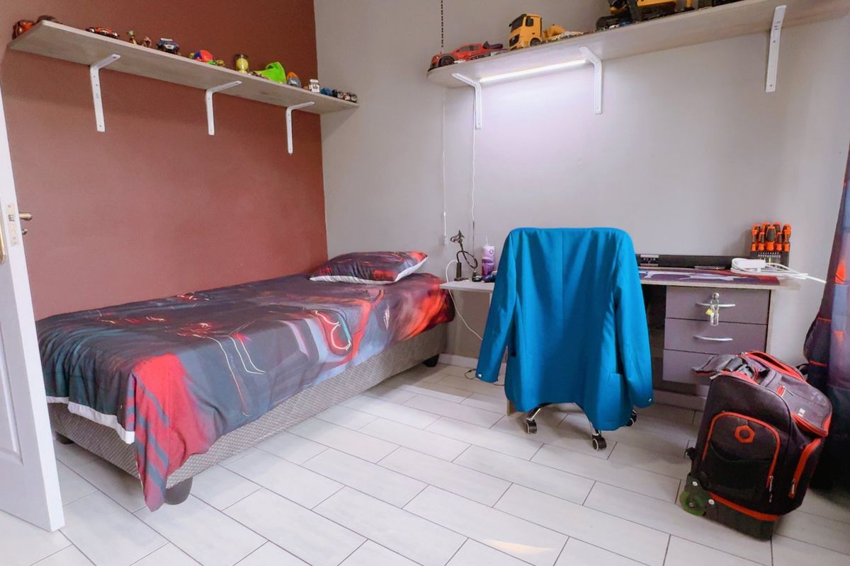 A functional bedroom featuring tiled flooring, built-in wall shelving, and a neutral color scheme with an accent wall.