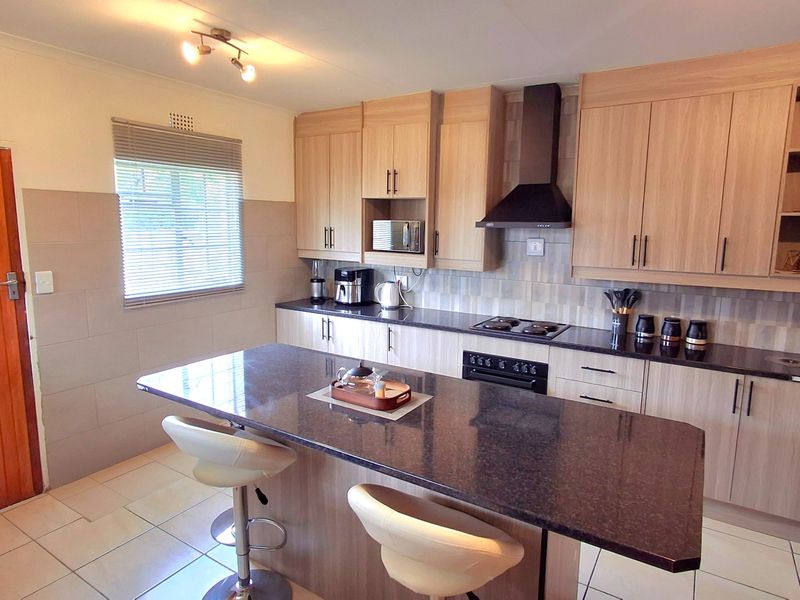 Modern kitchen featuring light wood cabinetry, dark granite countertops, a central island, and integrated appliances with a neutral tiled backsplash.