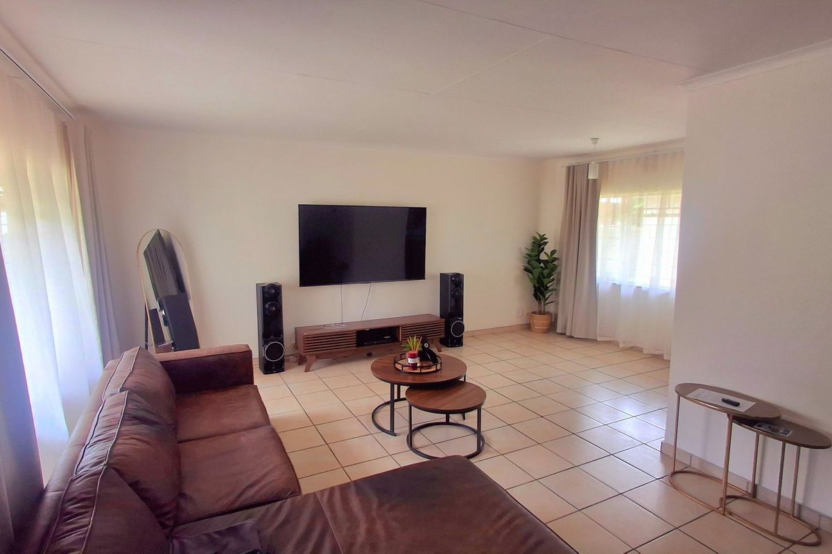 A spacious living room featuring neutral tiled flooring and large windows with curtain tracks, offering a bright and versatile living space.