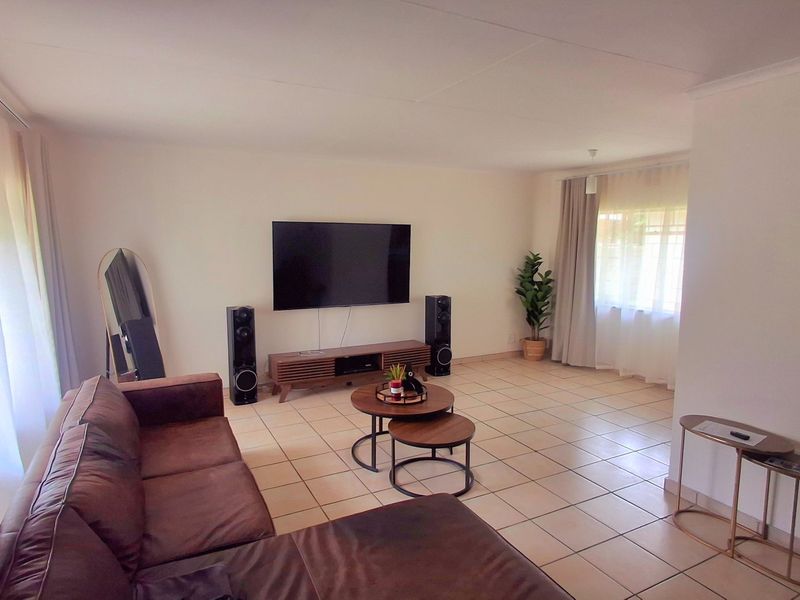 A spacious living room featuring neutral tiled flooring and large windows with curtain tracks, offering a bright and versatile living space.