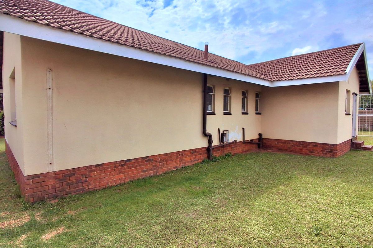 Rear exterior view of the house featuring a tiled roof, plastered walls with a brick plinth, and a security gate.