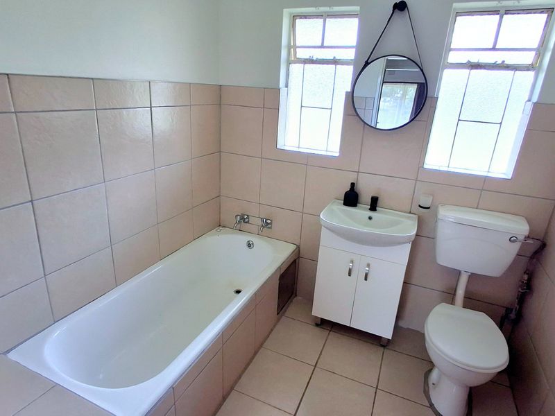 A functional bathroom featuring a bathtub, vanity cabinet with washbasin, and toilet, finished with neutral wall and floor tiles.