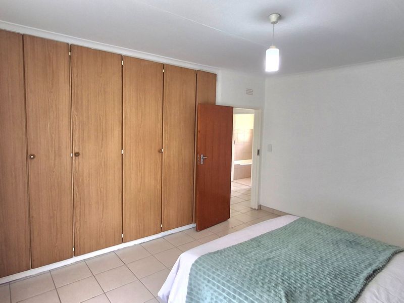 A bedroom featuring tiled flooring and extensive built-in wooden cupboards, with direct access to an adjoining bathroom.