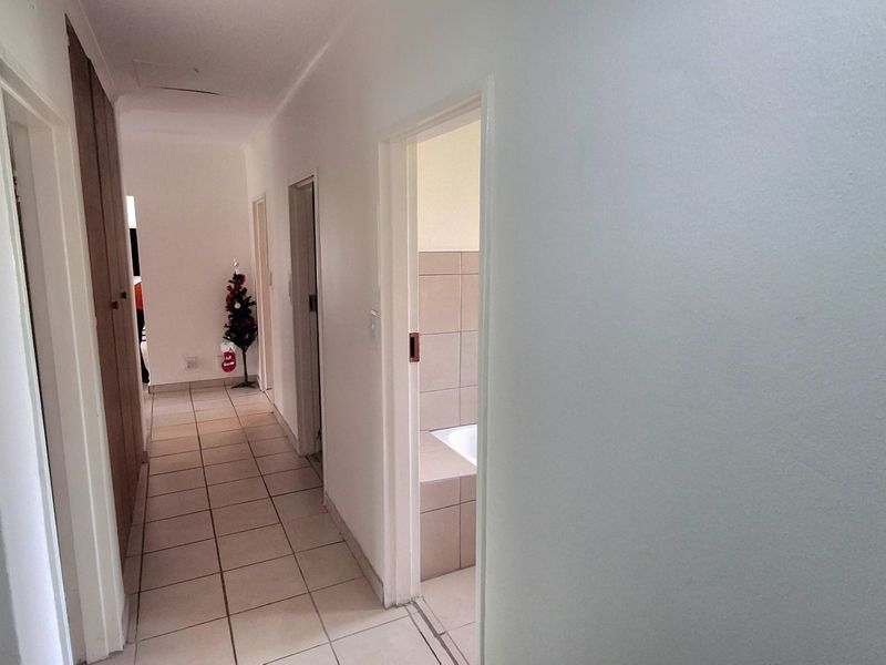 A clean, neutral hallway featuring tiled flooring and built-in storage cupboards, providing access to multiple rooms including a bathroom.