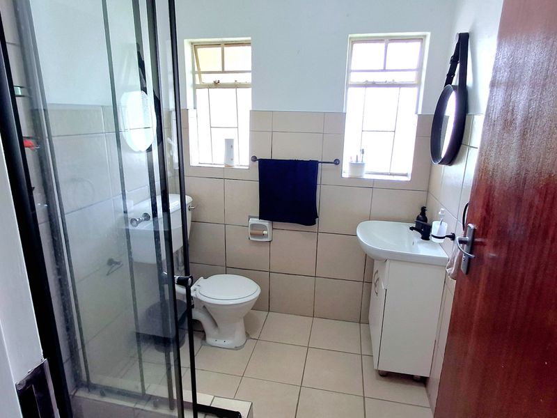 A functional bathroom featuring a shower enclosure, toilet, and vanity basin with neutral wall and floor tiling.