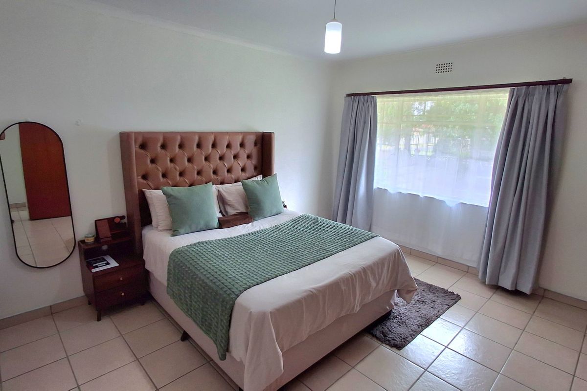 A well-lit bedroom featuring neutral tiled flooring and large windows with installed curtain rails, providing a clean and functional living space.