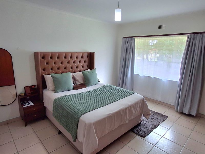 A well-lit bedroom featuring neutral tiled flooring and large windows with installed curtain rails, providing a clean and functional living space.
