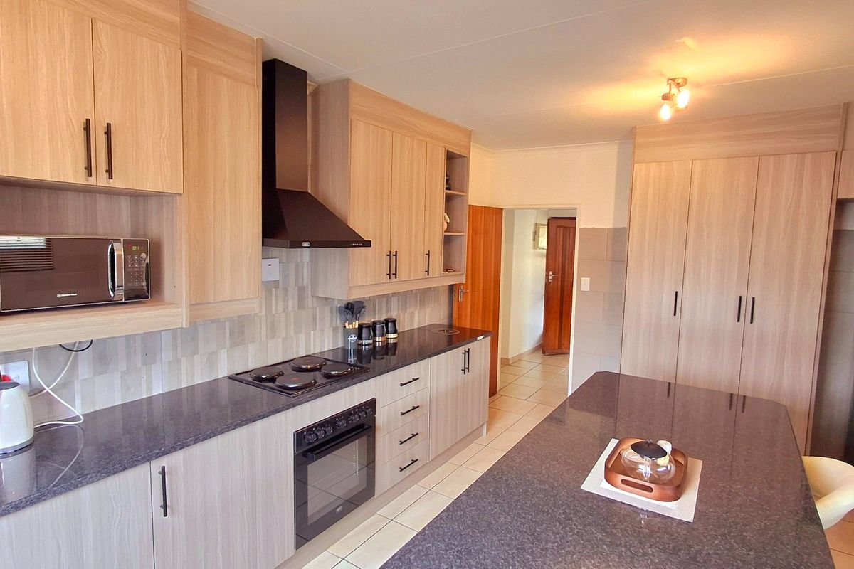 Modern kitchen featuring light wood cabinetry, dark granite countertops, built-in appliances, and tiled flooring, offering a clean and functional workspace.
