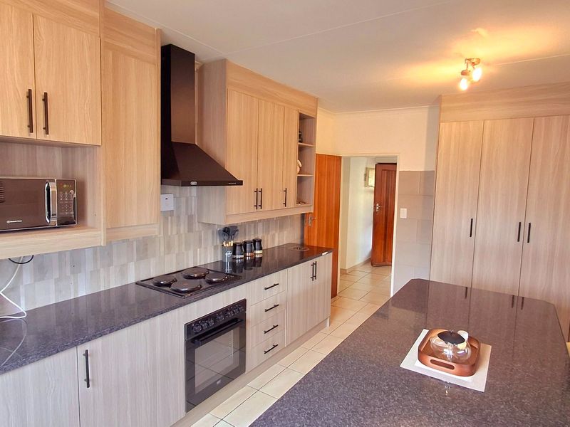Modern kitchen featuring light wood cabinetry, dark granite countertops, built-in appliances, and tiled flooring, offering a clean and functional workspace.