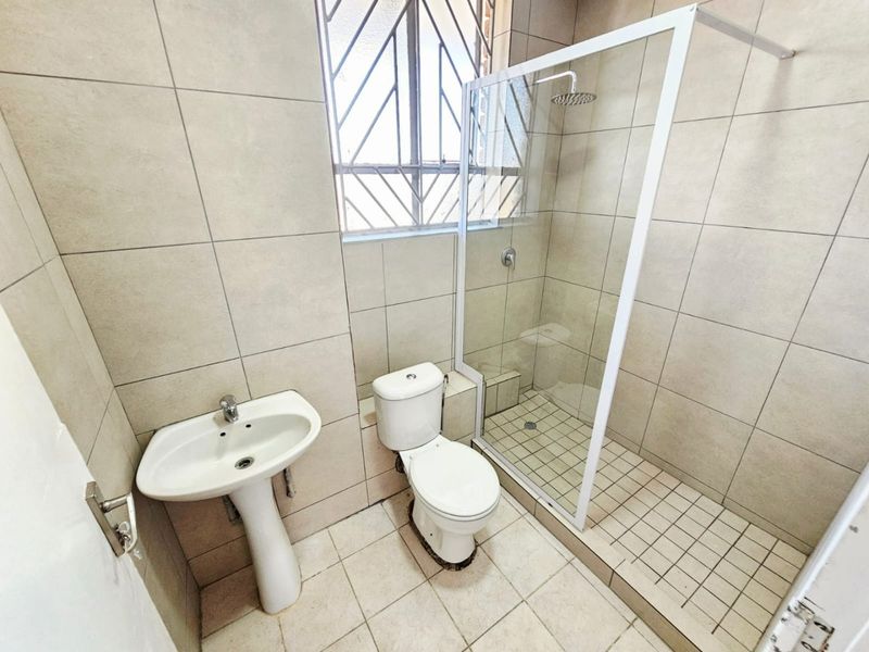 A clean, functional bathroom featuring a pedestal basin, toilet, and a walk-in shower with a glass enclosure and tiled finishes.