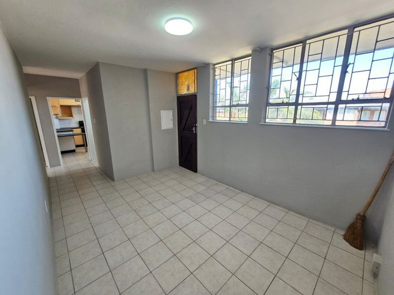 An empty living area featuring tiled flooring, security bars on the windows, and a view through to the kitchen area.