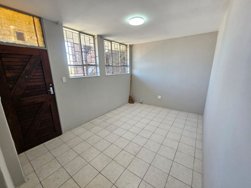 An empty bedroom featuring tiled flooring, security bars on the windows, and a wooden entrance door.