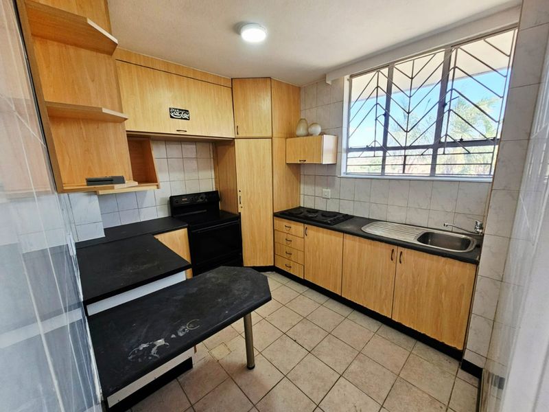 A functional kitchen featuring light wood-finish cabinetry, black countertops, a built-in oven and hob, and tiled flooring with a window providing natural light.