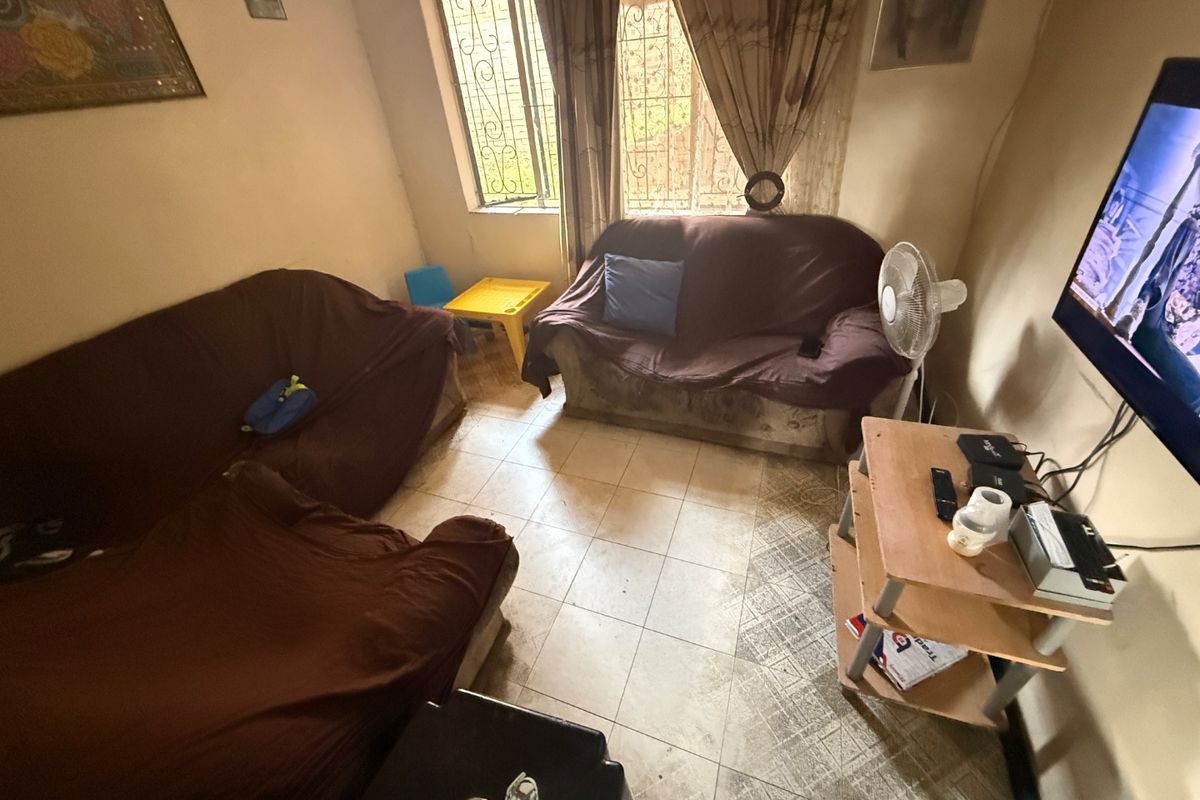 A compact living room featuring tiled flooring and a window with security bars, offering a functional space in need of cosmetic updates.
