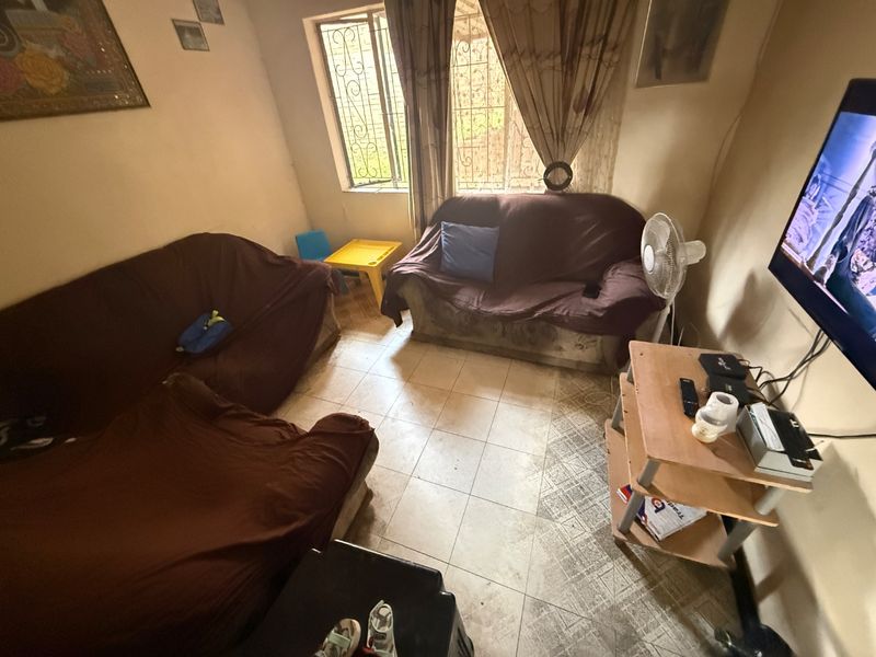 A compact living room featuring tiled flooring and a window with security bars, offering a functional space in need of cosmetic updates.