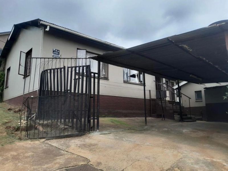 Front exterior view of the house featuring a concrete driveway, attached carport, and security fencing with razor wire.