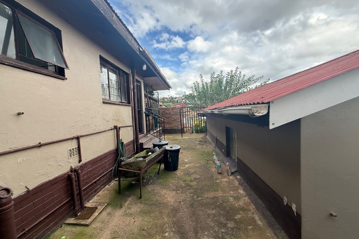 Rear exterior view of the property showing concrete paving, corrugated roofing, and external wall finishes requiring maintenance.