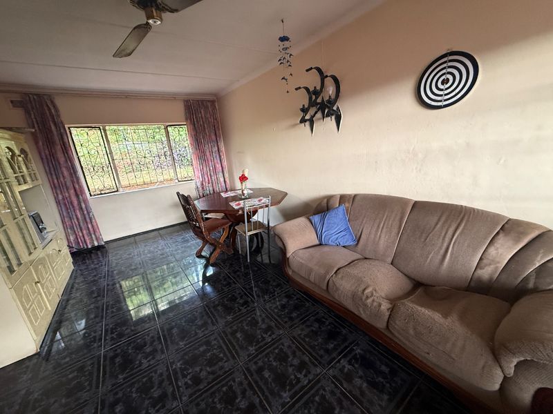 A living room featuring dark tiled flooring, a ceiling fan, and security bars on the window, offering a functional and dated living space.